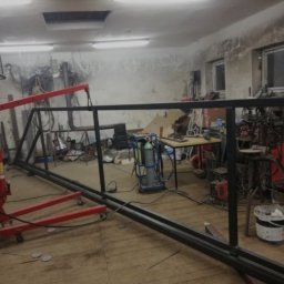 PRO SPAW - Warsztatowa sceneria z fragmentem konstrukcji metalowej w trakcie tworzenia. Widoczny sprzęt spawalniczy i inne narzędzia ślusarskie w tle.