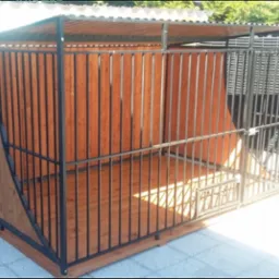 Konstrukcja metalowa z drewnianym wypełnieniem, prawdopodobnie kojec dla zwierząt, z zadaszeniem i kratami, widok z boku, na zewnątrz.