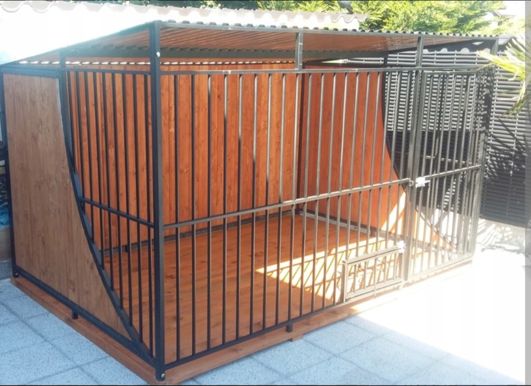 Konstrukcja metalowa z drewnianym wypełnieniem, prawdopodobnie kojec dla zwierząt, z zadaszeniem i kratami, widok z boku, na zewnątrz.