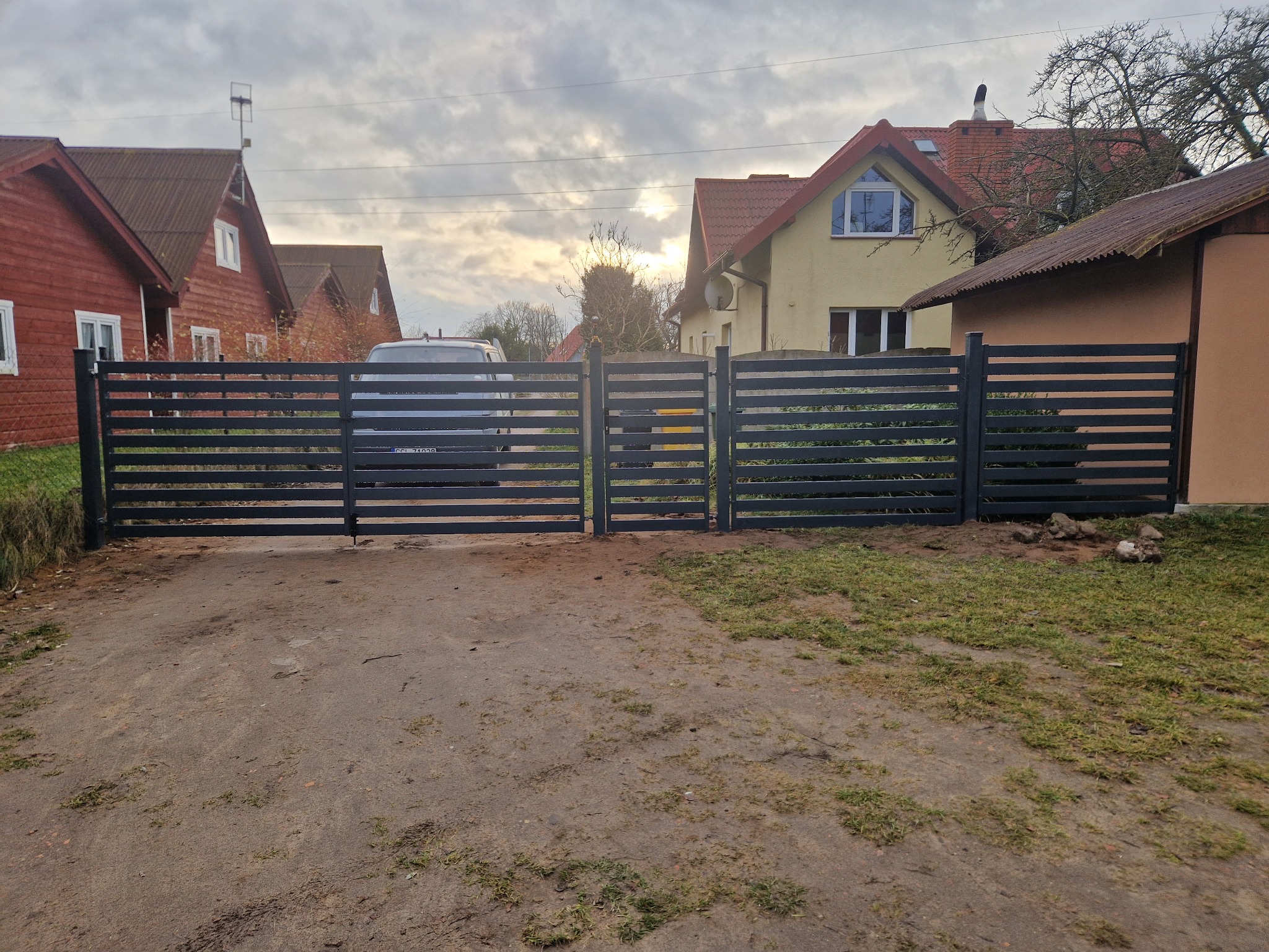Nowoczesna, pozioma brama wjazdowa w kolorze grafitowym, z widocznym samochodem w tle. Brama zamontowana przed domami jednorodzinnymi.