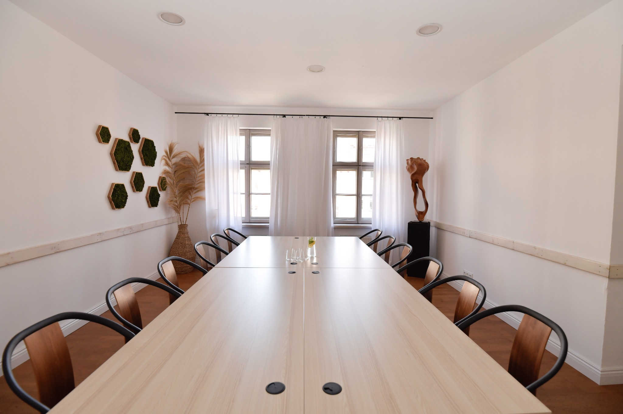 Sala konferencyjna z długim stołem, krzesłami, dekoracjami ściennymi i rzeźbą, idealna na spotkania biznesowe i szkolenia.