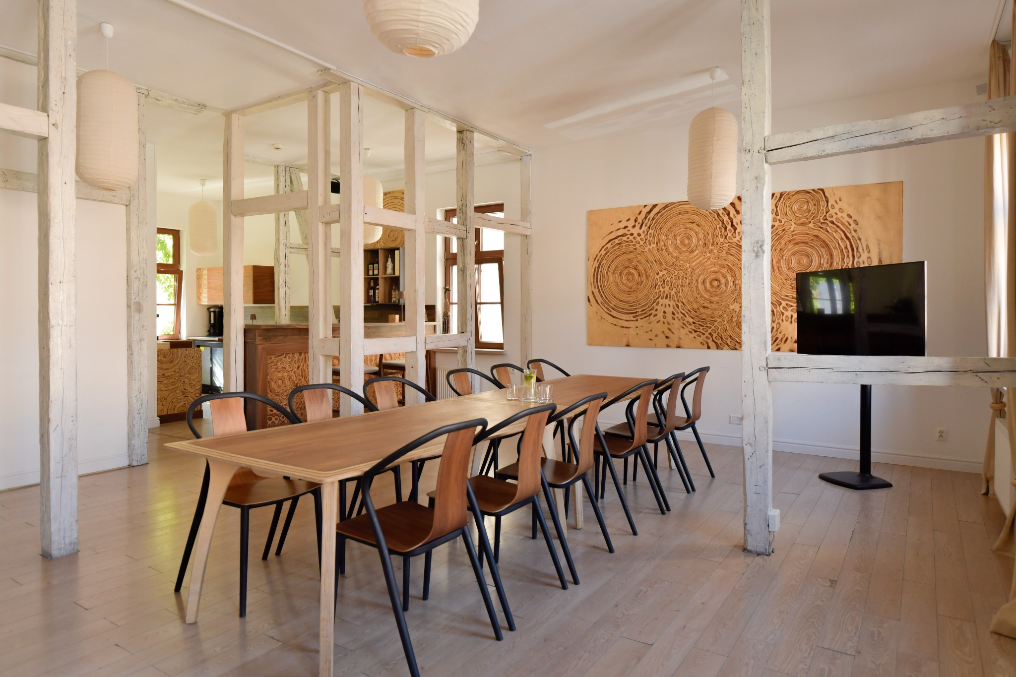 Sala konferencyjna z drewnianym stołem i krzesłami w jasnym wnętrzu, dekorowana lampami i obrazami, Poznań. Idealna na kameralne spotkania.