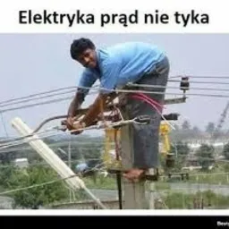 Mężczyzna na słupie energetycznym, naprawiający przewody elektryczne. Widok na otoczenie z zielenią. Ujęcie z dołu, podkreślające wysokość pracy.