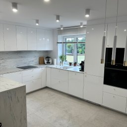 Lucas Dołhań - Nowoczesna, jasna kuchnia z białymi, lakierowanymi frontami, marmurowym blatem i wyspą. Minimalistyczne oświetlenie punktowe i wiszące lampy. Okno z widokiem na zieleń.