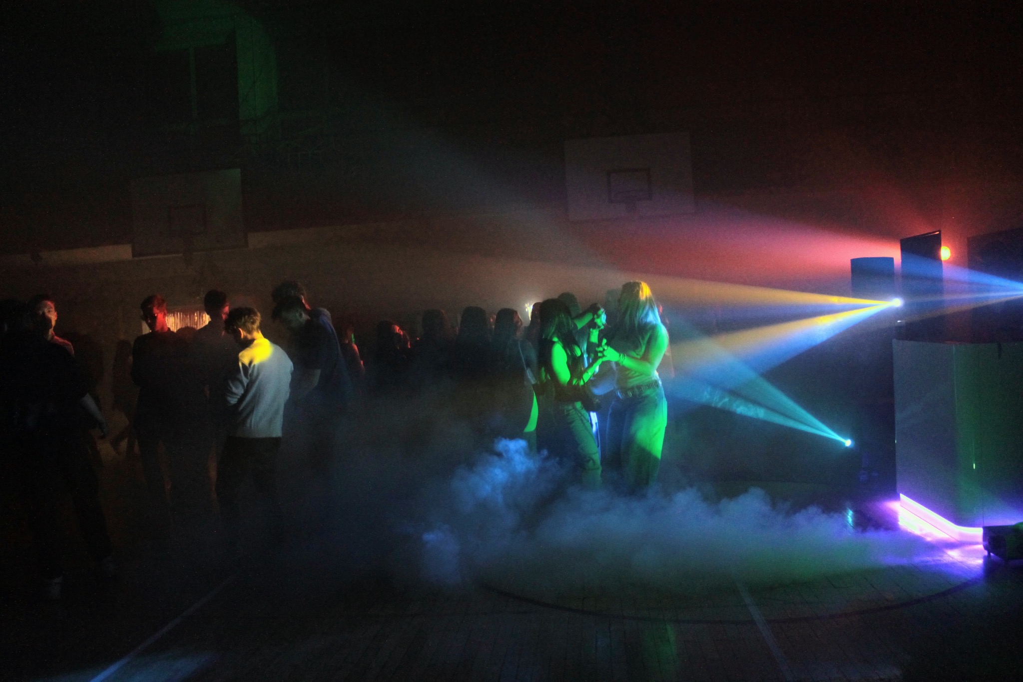 Zespół muzyczny na scenie podczas koncertu w hali sportowej, oświetlonej kolorowymi światłami i z dymem scenicznym.