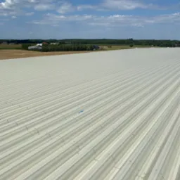 Szeroki, blaszany dach z wyraźnymi liniami w Zduńskiej Woli. Widok z góry, w tle błękitne niebo z chmurami i fragment krajobrazu. Nowoczesne pokrycie.