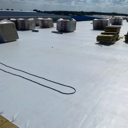 Daniel-Bud Grobelny Daniel - Biała membrana dachowa z izolacją termiczną Rockwool w pakietach i kablami, przygotowana do montażu na płaskim dachu w słoneczny dzień.