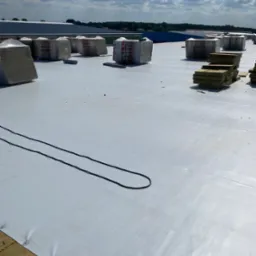 Biała membrana dachowa z izolacją termiczną Rockwool w pakietach i kablami, przygotowana do montażu na płaskim dachu w słoneczny dzień.