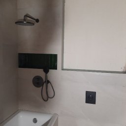 Mykola Dushuk - Wykończona łazienka z beżowymi płytkami, czarną armaturą, zieloną wnęką nad wanną i podtynkową toaletą. Widoczne detale i elementy wyposażenia.