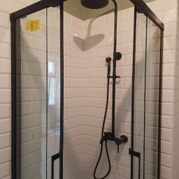 Mykola Dushuk - Nowoczesna kabina prysznicowa z czarną armaturą na tle białych płytek imitujących cegłę, widok z narożnika. Minimalistyczny design i funkcjonalność.