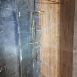 Mykola Dushuk - Nowoczesna kabina prysznicowa z deszczownicą w odcieniach szarości i drewna, oddzielona szklaną ścianką. Widoczne półki wkomponowane w ścianę.