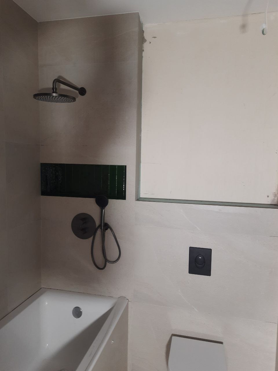 Wykończona łazienka z beżowymi płytkami, czarną armaturą, zieloną wnęką nad wanną i podtynkową toaletą. Widoczne detale i elementy wyposażenia.