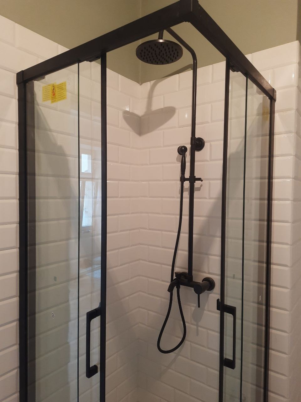 Nowoczesna kabina prysznicowa z czarną armaturą na tle białych płytek imitujących cegłę, widok z narożnika. Minimalistyczny design i funkcjonalność.