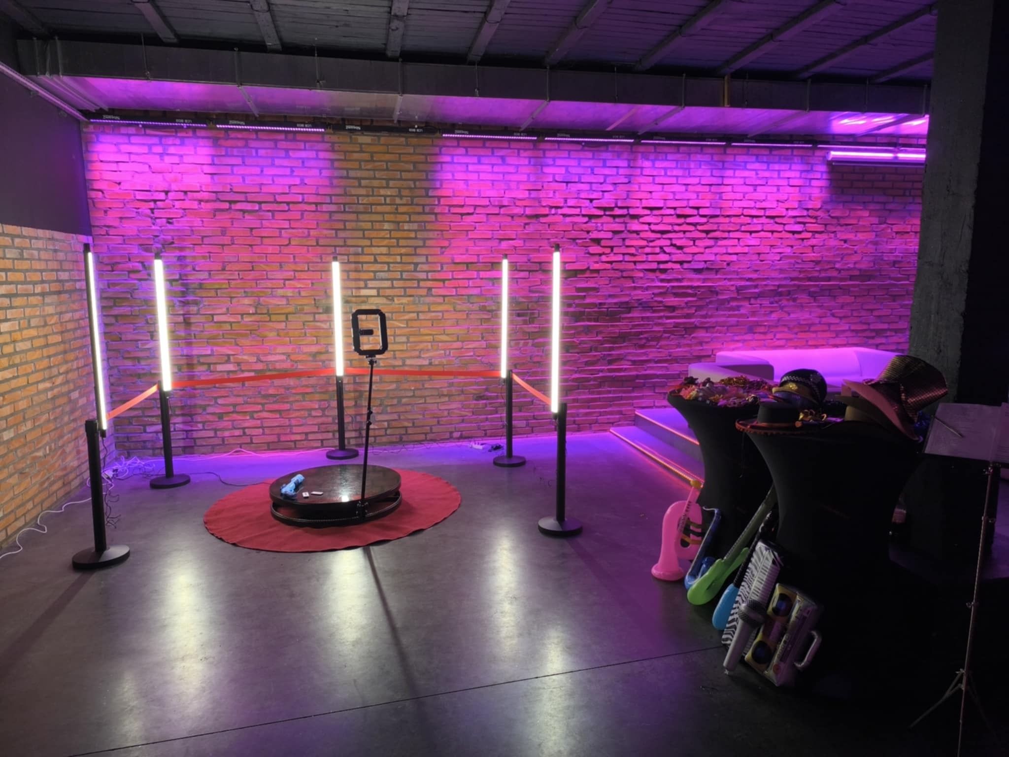 Stanowisko z obrotową platformą i rekwizytami na tle ceglanej ściany oświetlonej fioletowym światłem. Przygotowane do sesji zdjęciowej.