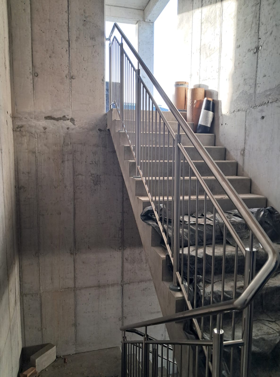 Surowe schody betonowe z zamontowaną, nowoczesną poręczą ze stali nierdzewnej w jasnym, industrialnym wnętrzu budynku w trakcie budowy.