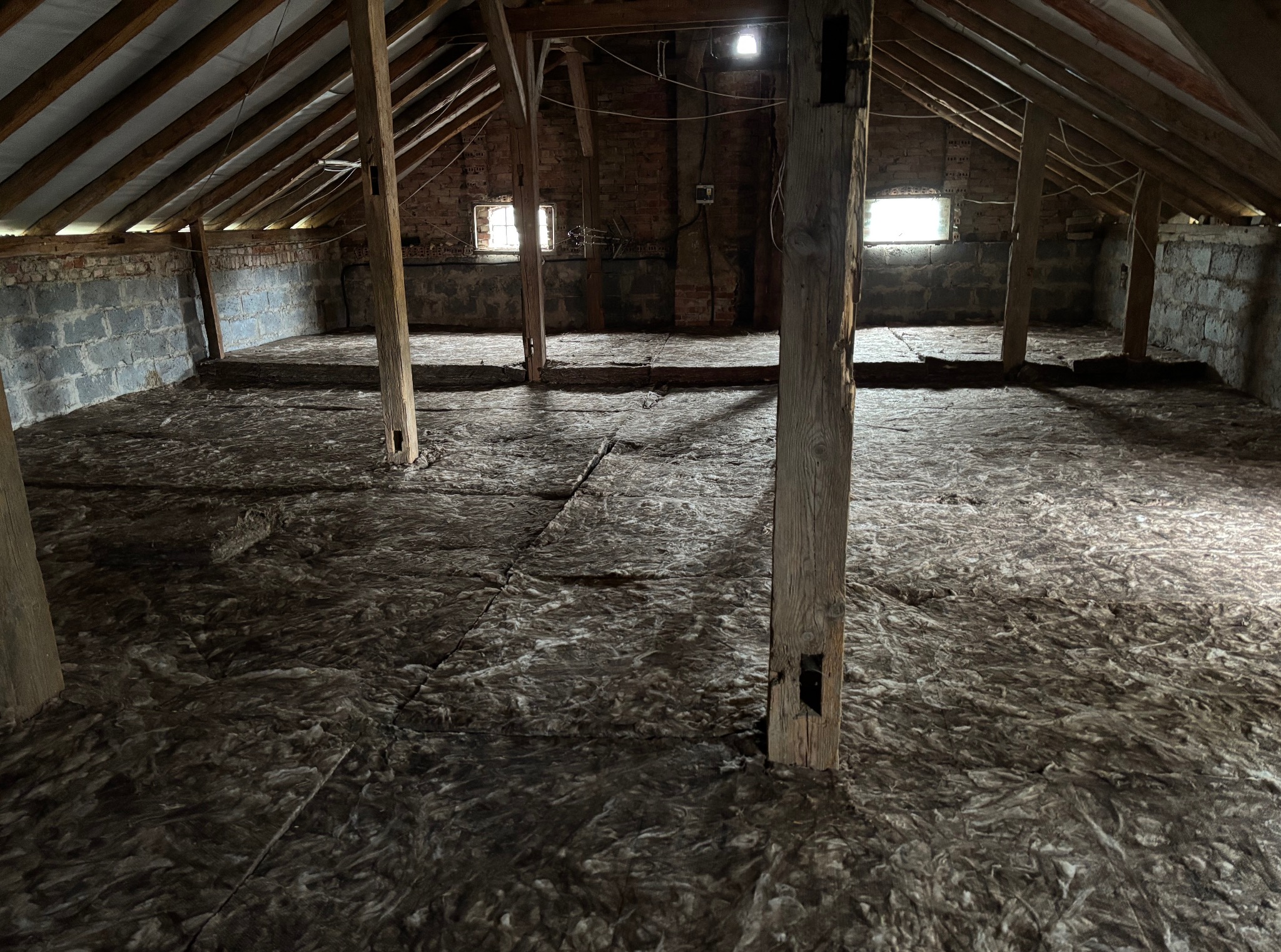 Poddasze z odsłoniętą konstrukcją i ociepleniem z wełny mineralnej, widoczne drewniane słupy. Ocieplenie poddasza w surowym wnętrzu.