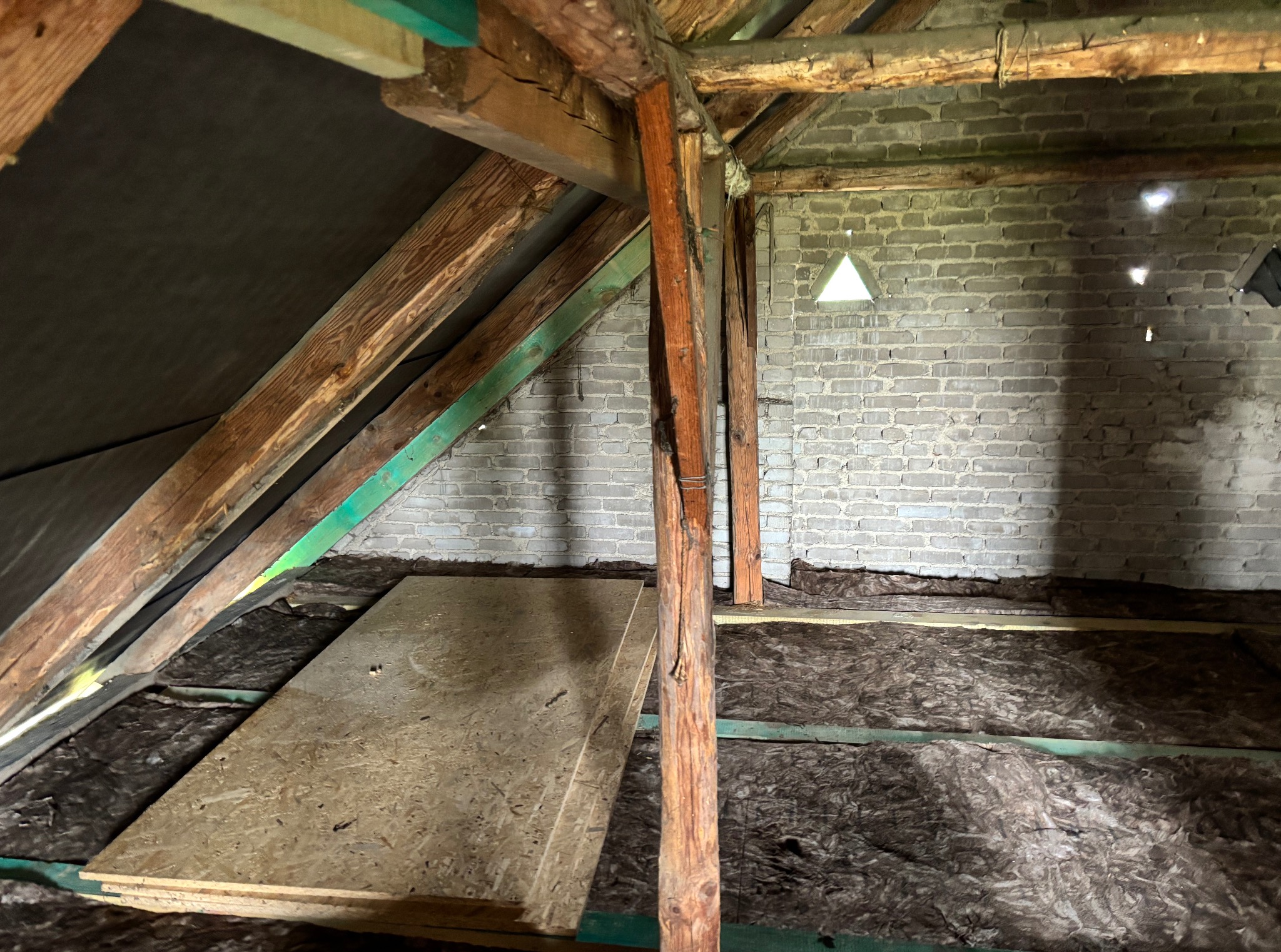 Poddasze w trakcie ocieplania: wełna mineralna między krokwiami, płyta OSB, ściana z cegły z trójkątnym okienkiem. Widoczne drewniane elementy konstrukcyjne.