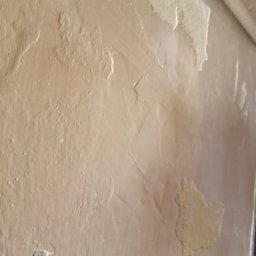 Artur Michalak - Niedokładne, beżowe szpachlowanie ściany z widocznymi, odspojonymi fragmentami starej farby i nierównościami. Widoczne ślady po pędzlu.