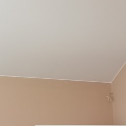 Artur Michalak - Jasny pokój po odświeżeniu: beżowe ściany, biały sufit i fragment białych drzwi. Widoczny narożnik pokoju i kabel wystający ze ściany.