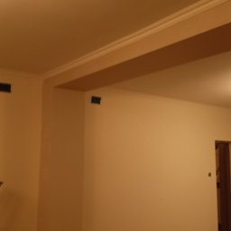 Artur Michalak - Świeżo pomalowane ściany w odcieniach beżu z listwami dekoracyjnymi w Grójcu. Zabezpieczona podłoga folią malarską, widoczne ślady po taśmie malarskiej.