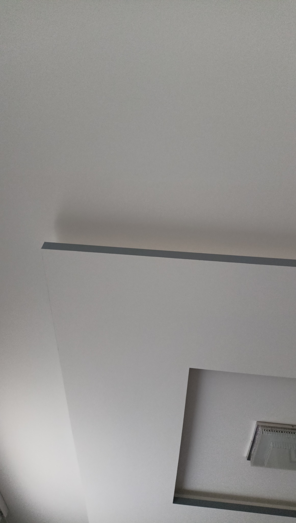 Nowoczesny sufit podwieszany z oświetleniem LED, wykończony gładzią w odcieniach bieli i szarości. Minimalistyczny design, kątowe ujęcie z dołu.