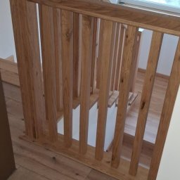 Roman Pasecki - Nowoczesne schody z jasnego drewna z balustradą w minimalistycznym stylu. Widoczne drewniane panele podłogowe i białe ściany. Okno w tle wpuszcza naturalne światło.