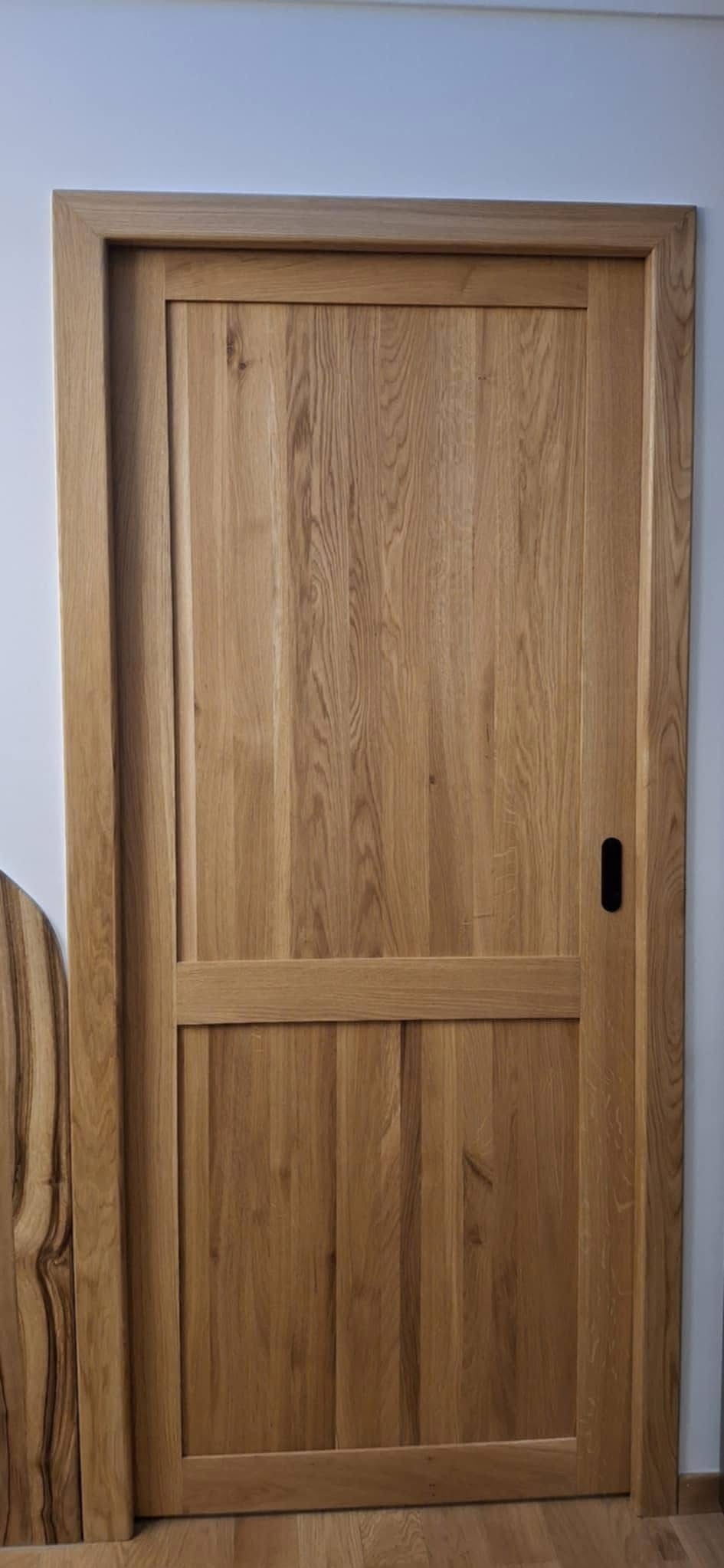 Dębowa, wewnętrzna stolarka drzwiowa z czarnym, minimalistycznym uchwytem, prezentująca naturalne usłojenie drewna i precyzję wykonania.