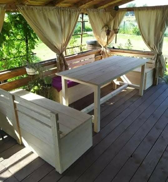 Drewniana altana z zasłonami, stół i ławki z surowego drewna na tarasie. Widok na zieleń w tle. Naturalne światło.