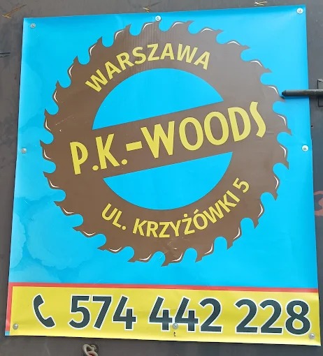 Błękitny baner reklamowy firmy P.K.-WOODS z Warszawy, z brązowym logo piły tarczowej i żółtym numerem telefonu na dole. Baner zawieszony na metalowych oczkach.