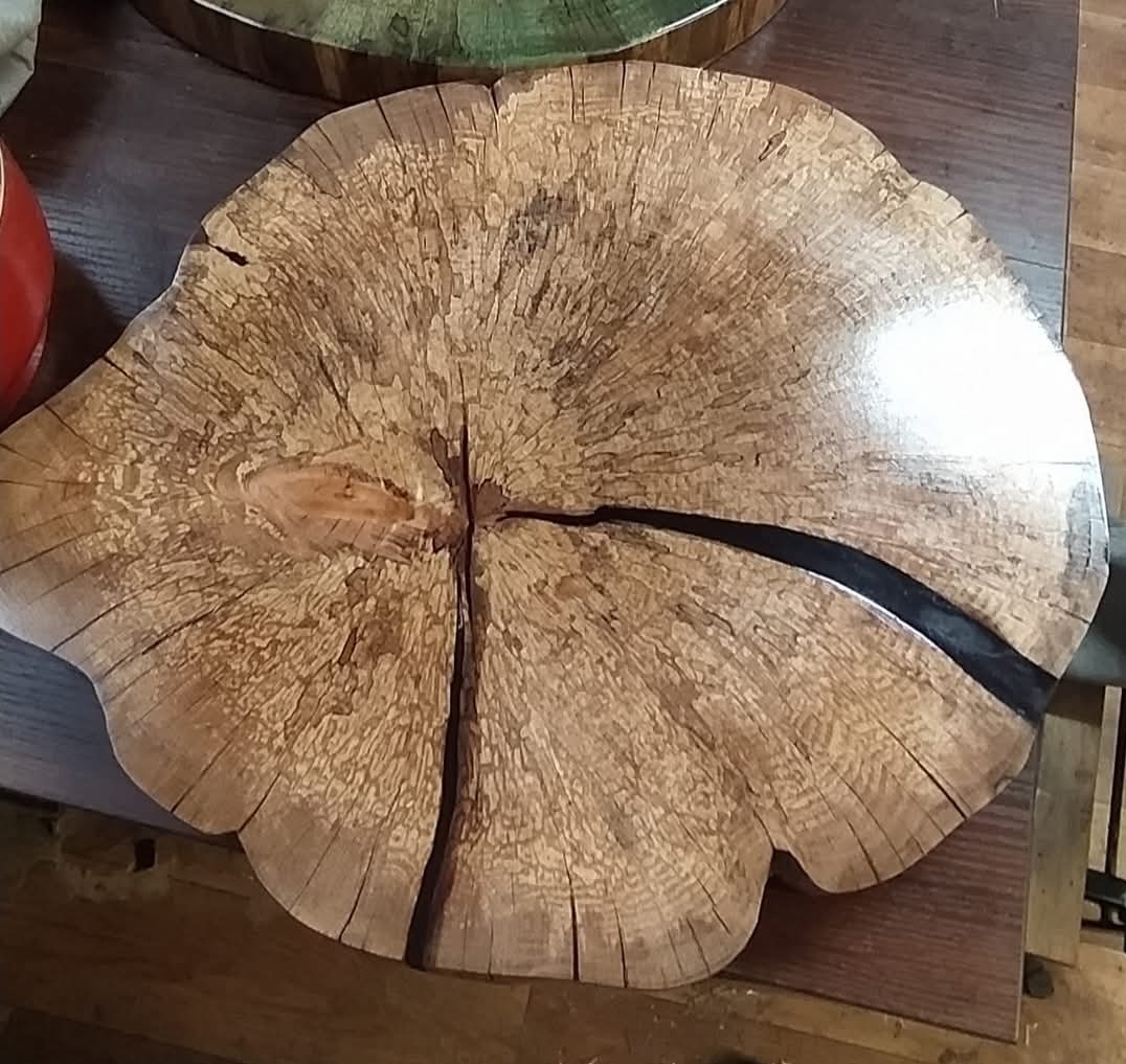 Unikatowy plaster drewna z żywicą epoksydową wypełniającą pęknięcia, ukazujący naturalne słoje i teksturę drewna na ciemnym tle. Widoczne detale obróbki.