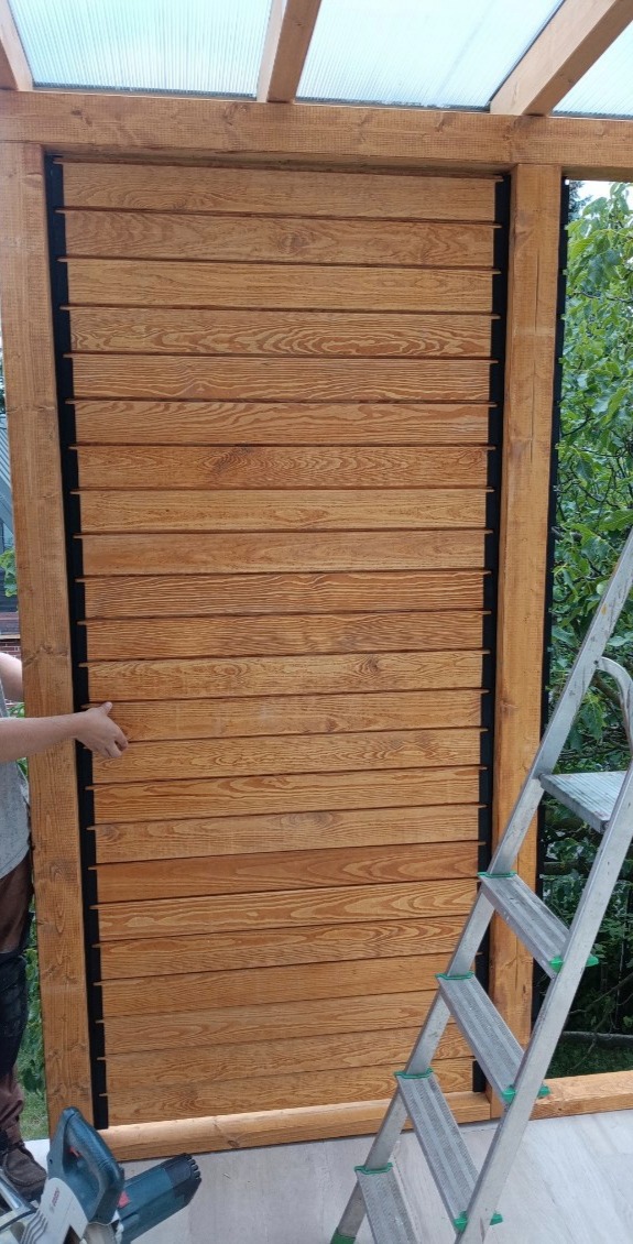 Montaż drewnianej konstrukcji z poziomych desek, widoczna drabina i narzędzia. Element zabudowy z naturalnego drewna w trakcie instalacji.