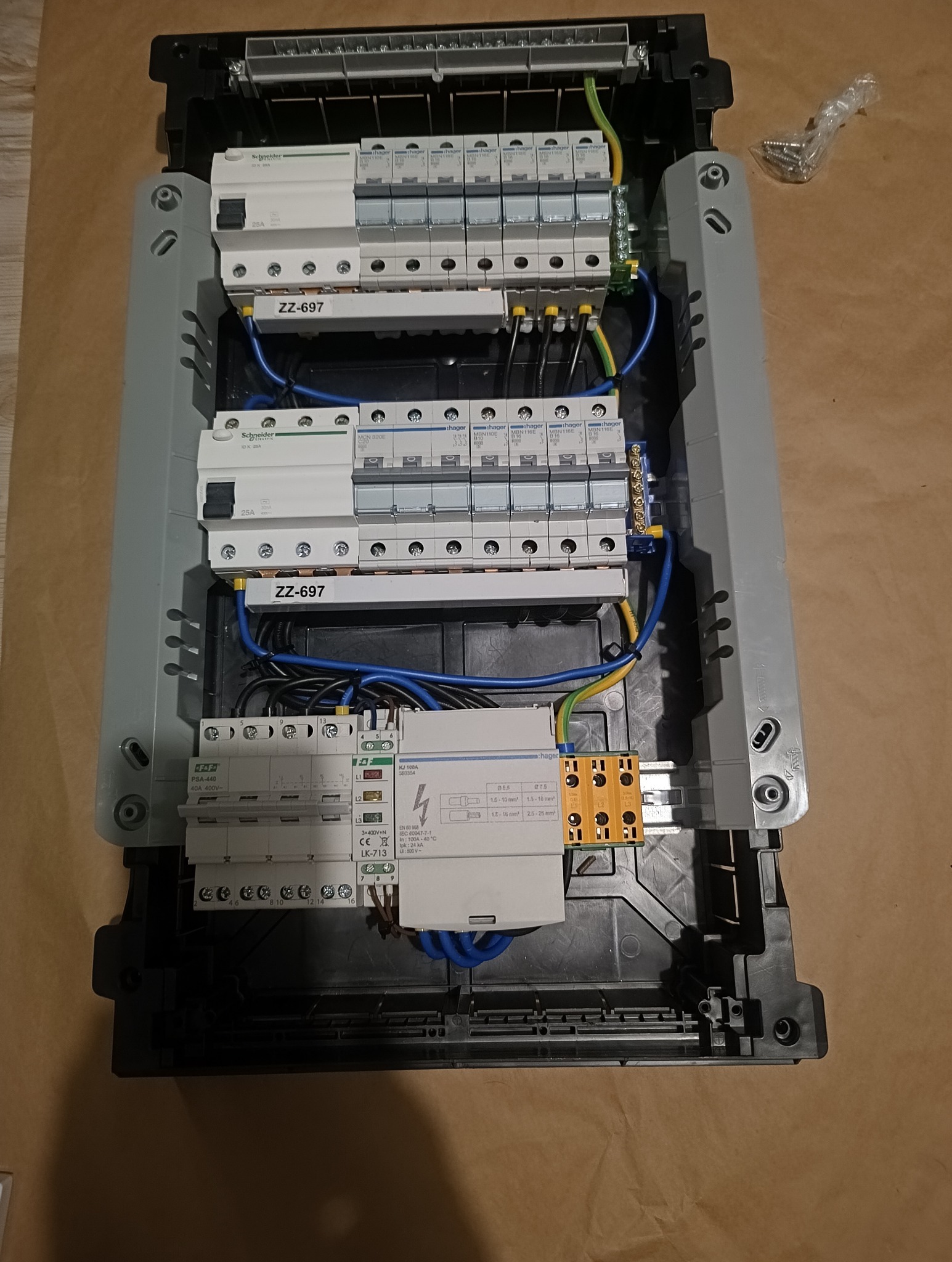 Rozdzielnica elektryczna z zamontowanymi bezpiecznikami, przewodami i modułami, widok z góry. Widoczne elementy marki Schneider i Hager. Przewody ułożone wewnątrz obudowy.