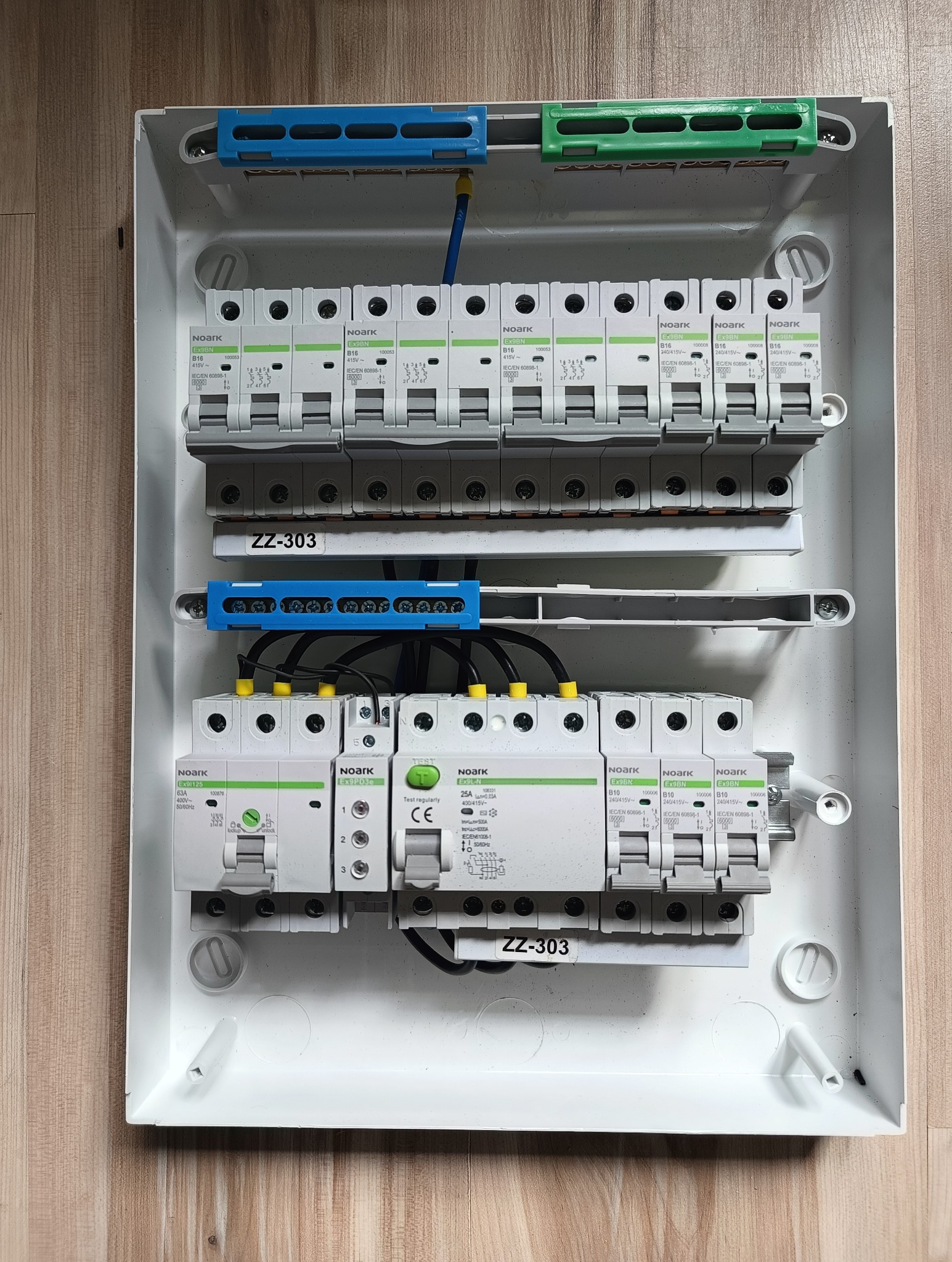 Rozdzielnica elektryczna z zamontowanymi bezpiecznikami Noark, widok z góry, przewody podłączone, oznaczenie ZZ-303 na obudowie.