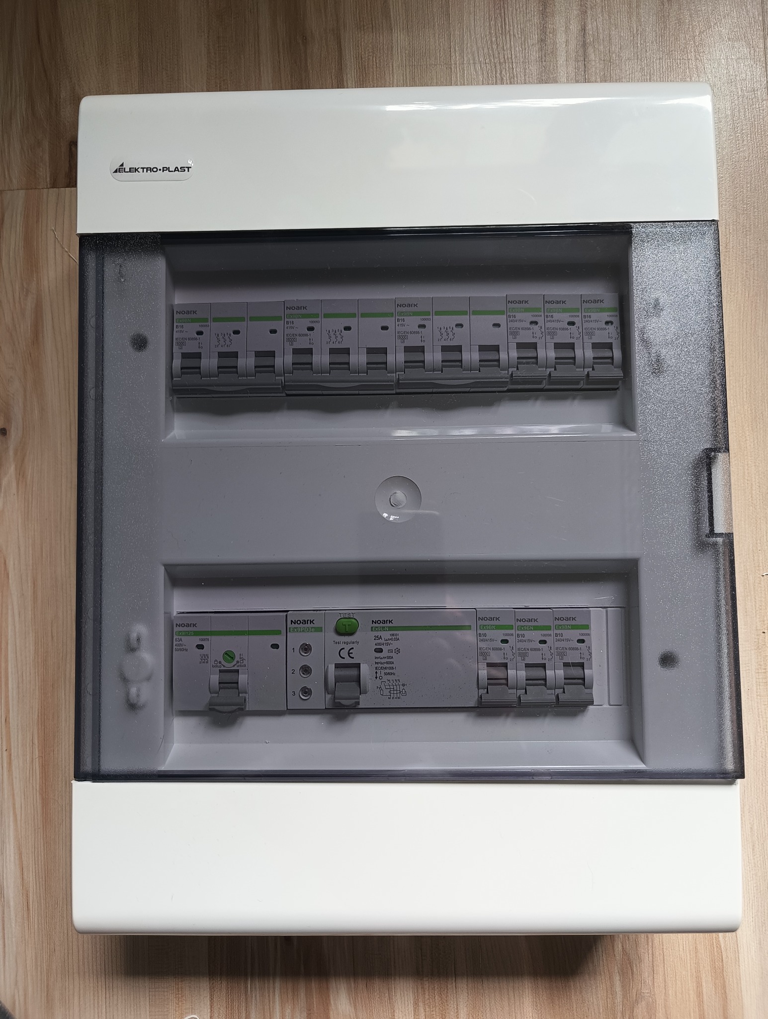 Rozdzielnica elektryczna natynkowa marki Elektro-Plast z zainstalowanymi bezpiecznikami Noark, widoczna na drewnianej powierzchni z bliska.