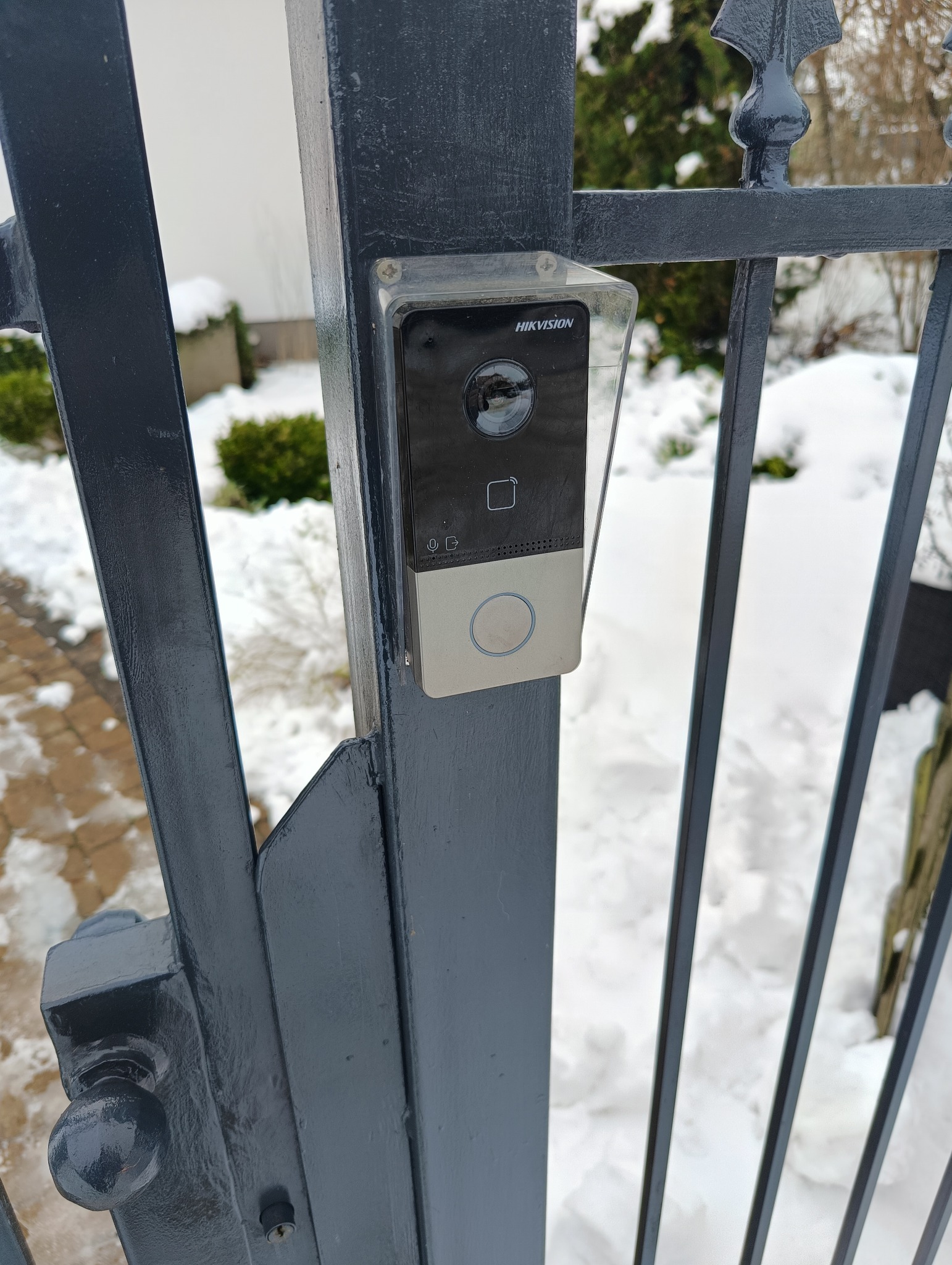 Zamontowany wideodomofon Hikvision na metalowej bramie w Subkowach. Widoczna kamera, czytnik kart i przycisk dzwonka. Zimowy krajobraz w tle.
