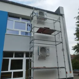 Montaż dwóch klimatyzatorów Fujitsu Airstage na elewacji budynku z pomocą rusztowania. Widoczne okna i rynna.