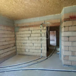 Surowy stan: instalacja ogrzewania podłogowego w domu jednorodzinnym. Rury grzewcze ułożone na posadzce, przymocowane do ściany. Widoczne bloczki ceramiczne.