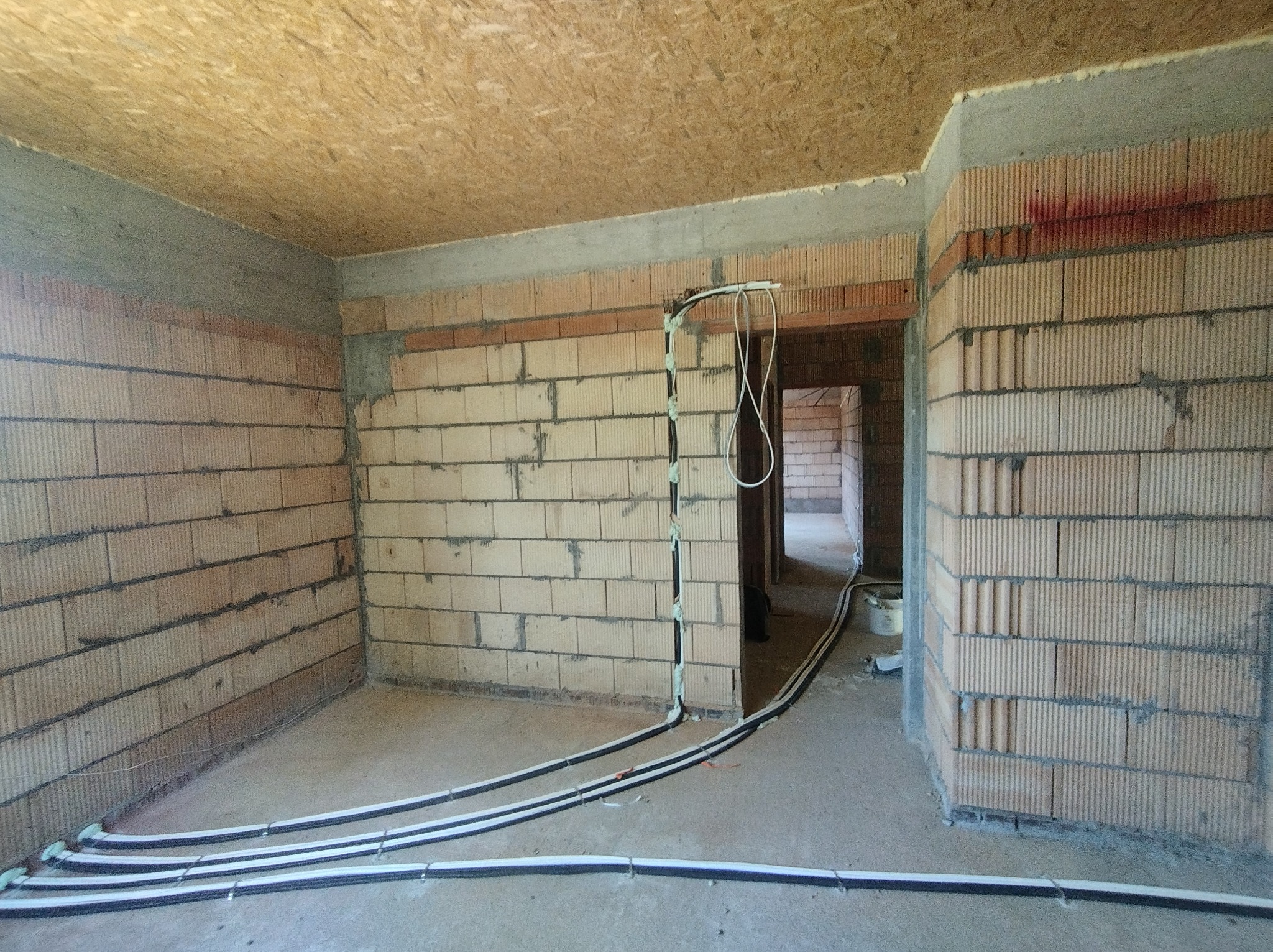 Surowy stan: instalacja ogrzewania podłogowego w domu jednorodzinnym. Rury grzewcze ułożone na posadzce, przymocowane do ściany. Widoczne bloczki ceramiczne.