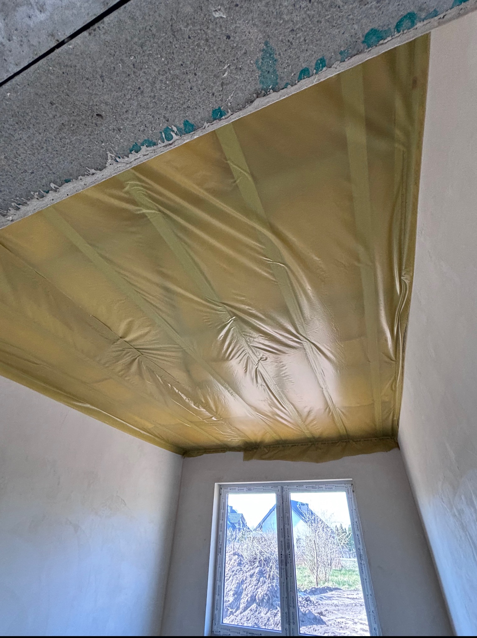 Żółta folia zabezpieczająca na suficie w trakcie remontu, widok z dołu, okno w tle. Zabezpieczenie przed malowaniem lub szpachlowaniem.