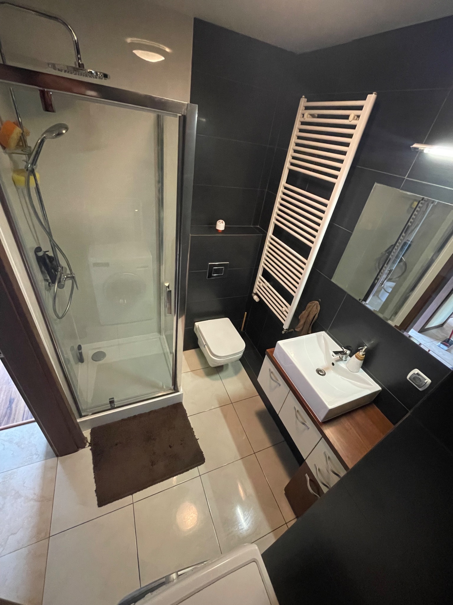 Nowoczesna łazienka w Skarbimierzycach z kabiną prysznicową, umywalką z szafką i grzejnikiem drabinkowym na tle czarnych płytek. Widok z góry.