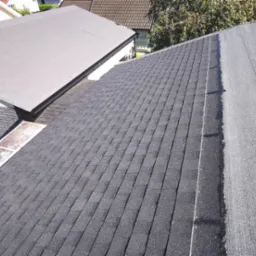 Fragment dachu z gontów bitumicznych i papy termozgrzewalnej. Widoczne połączenie dwóch różnych typów pokrycia dachowego. Ujęcie z góry, ostre światło słoneczne.