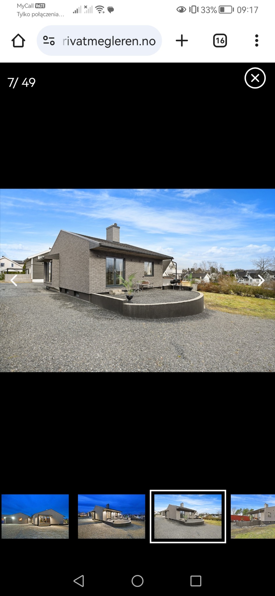 Nowoczesny dom z szarej cegły z płaskim dachem i kominem. Widoczny taras z meblami ogrodowymi i szara nawierzchnia. Błękitne niebo w tle.