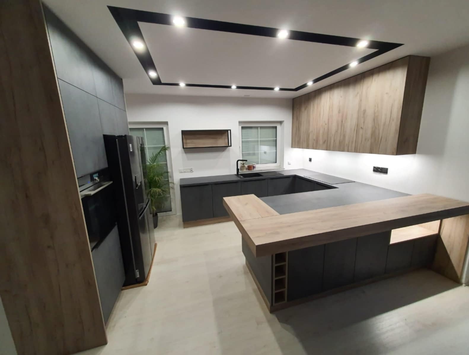 Nowoczesna kuchnia w odcieniach szarości i drewna z wyspą, podświetleniem LED podszafkowym i czarnymi akcentami sufitowymi. Minimalistyczny design.