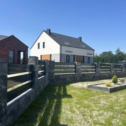 KBD Kacper Błaszczyk Design - Nowoczesne ogrodzenie panelowe z szarego kamienia łupanego, z poziomymi, metalowymi przęsłami, na tle domu jednorodzinnego i błękitnego nieba.