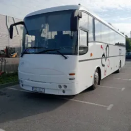Biały autokar z dekoracyjnym motywem parkuje na parkingu. Widoczny przód pojazdu z tablicą rejestracyjną i oznaczeniem 'Cieczka' nad przednią szybą.