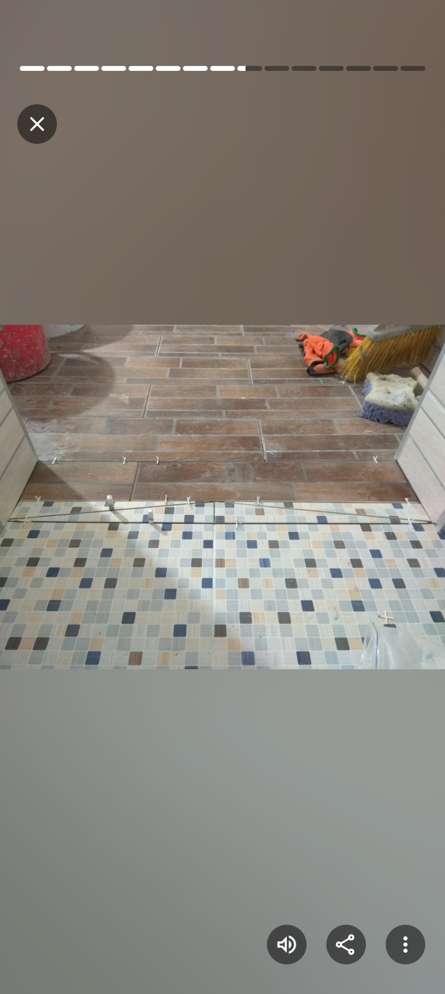 Fragment podłogi z brązowych płytek imitujących drewno i mozaiki w odcieniach szarości i błękitu, z widocznymi krzyżykami dystansowymi. W tle narzędzia i wiadro.