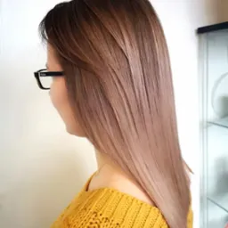 Uczesana, prosta fryzura z ombre w odcieniach brązu i blondu na włosach do ramion, widok z boku, kobieta w okularach i żółtym swetrze.