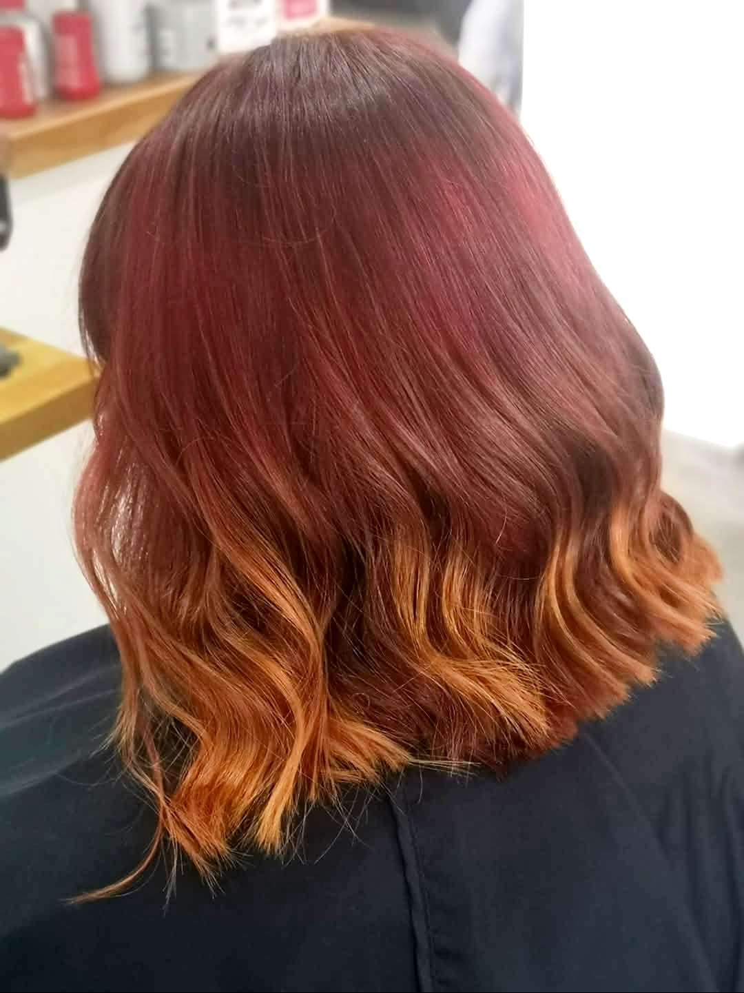 Cieniowane, falowane włosy w odcieniach czerwieni i miedzi, widoczne od tyłu. Efekt koloryzacji ombre na krótkich włosach, z ciemniejszą górą i jaśniejszym dołem.
