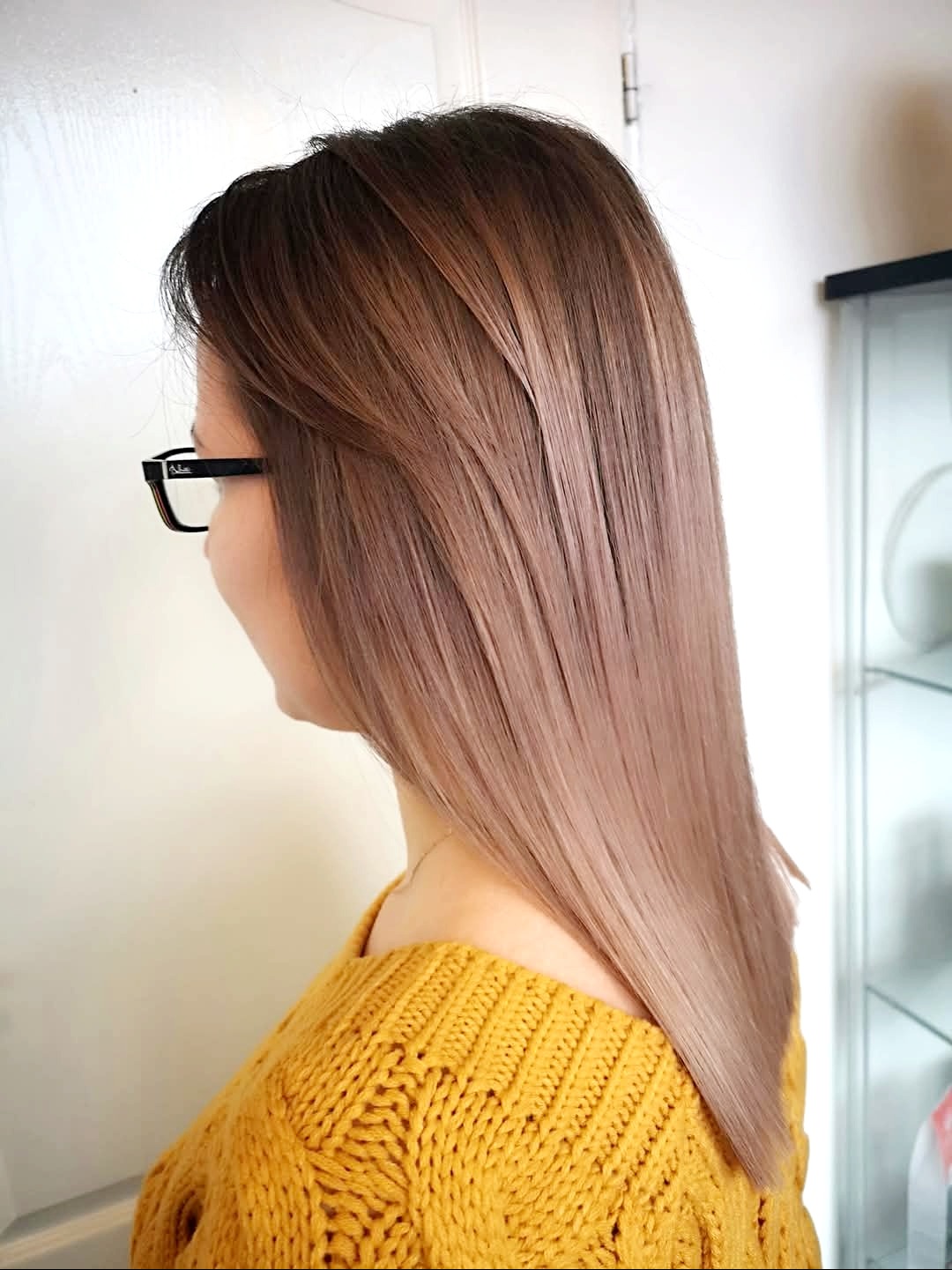 Uczesana, prosta fryzura z ombre w odcieniach brązu i blondu na włosach do ramion, widok z boku, kobieta w okularach i żółtym swetrze.