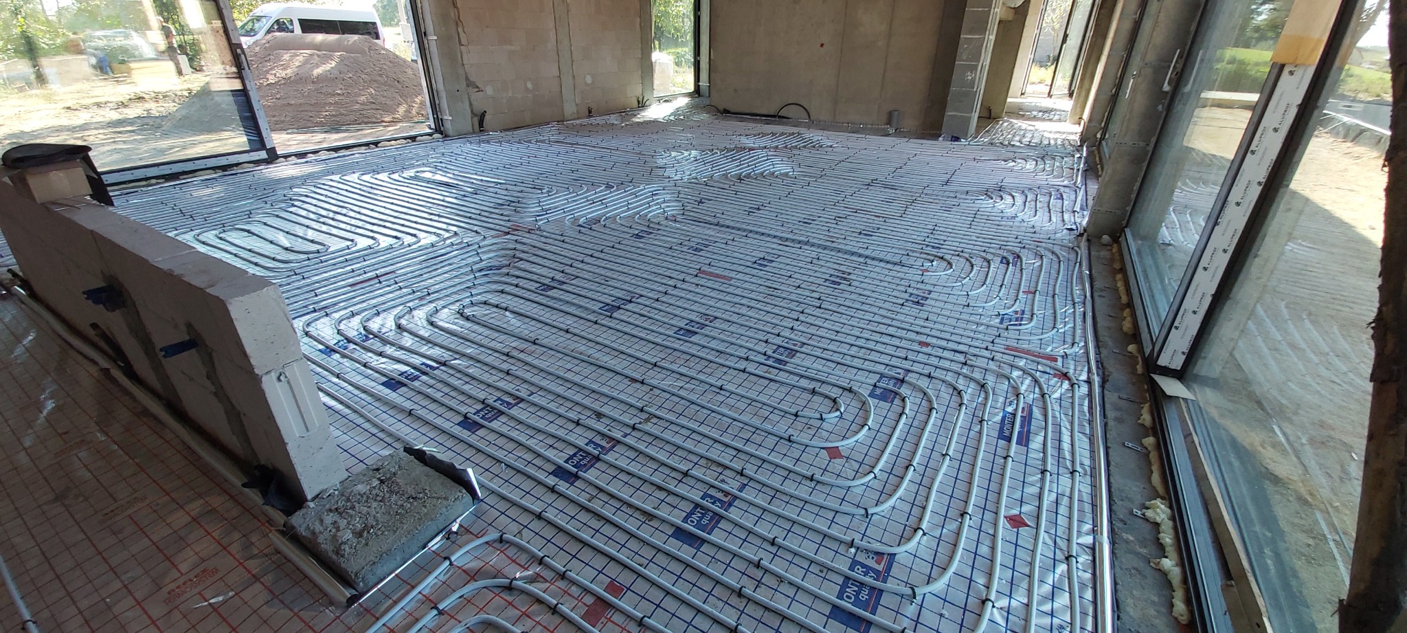 Białe rury ogrzewania podłogowego ułożone zygzakiem na folii w surowym wnętrzu, widok z góry, Warszawa. Instalacja przed wylaniem posadzki.